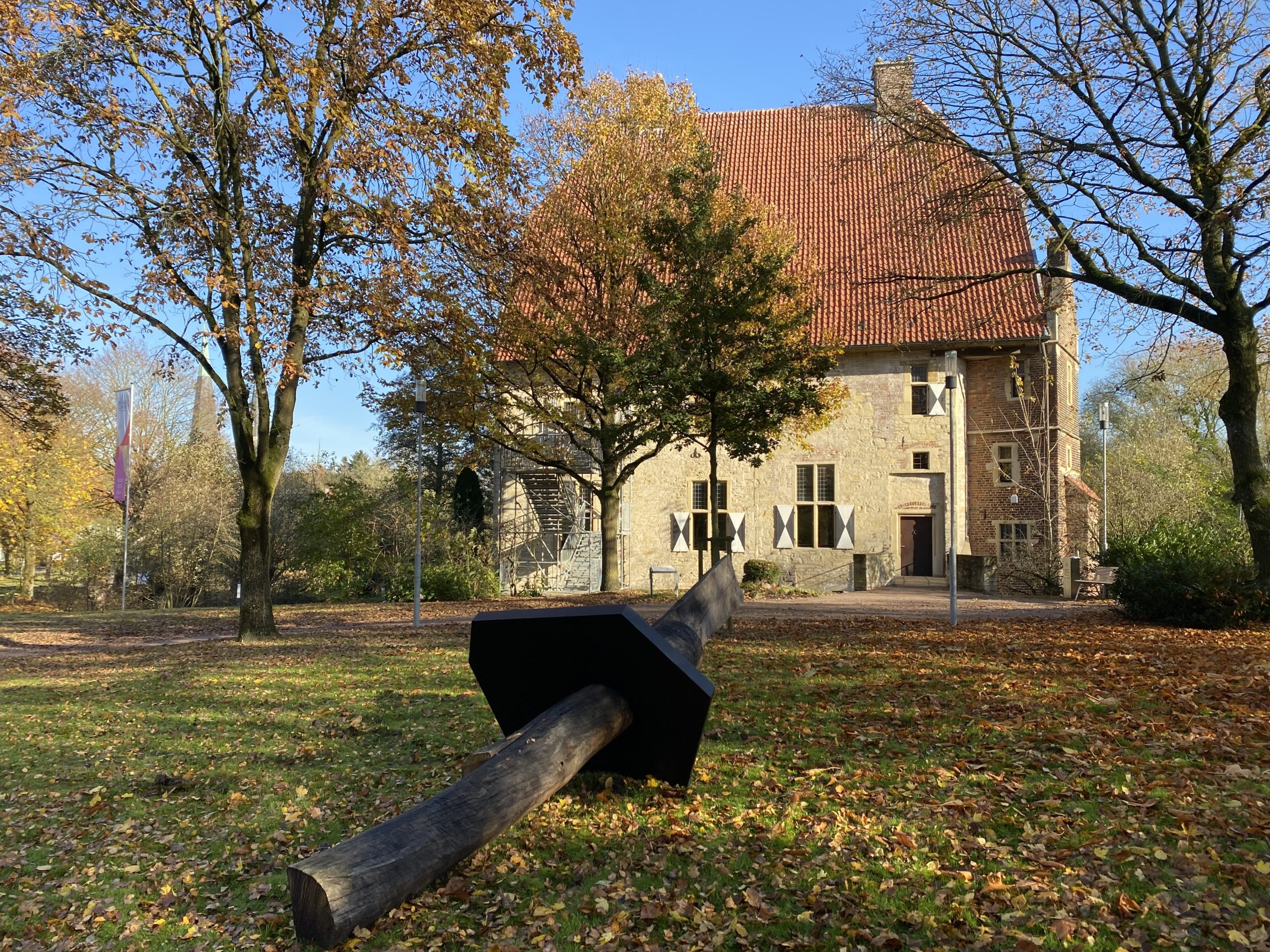 Holzskulptur "One Plate" auf der Wiese vor der historischen Kolvenburg und blauem Himmel